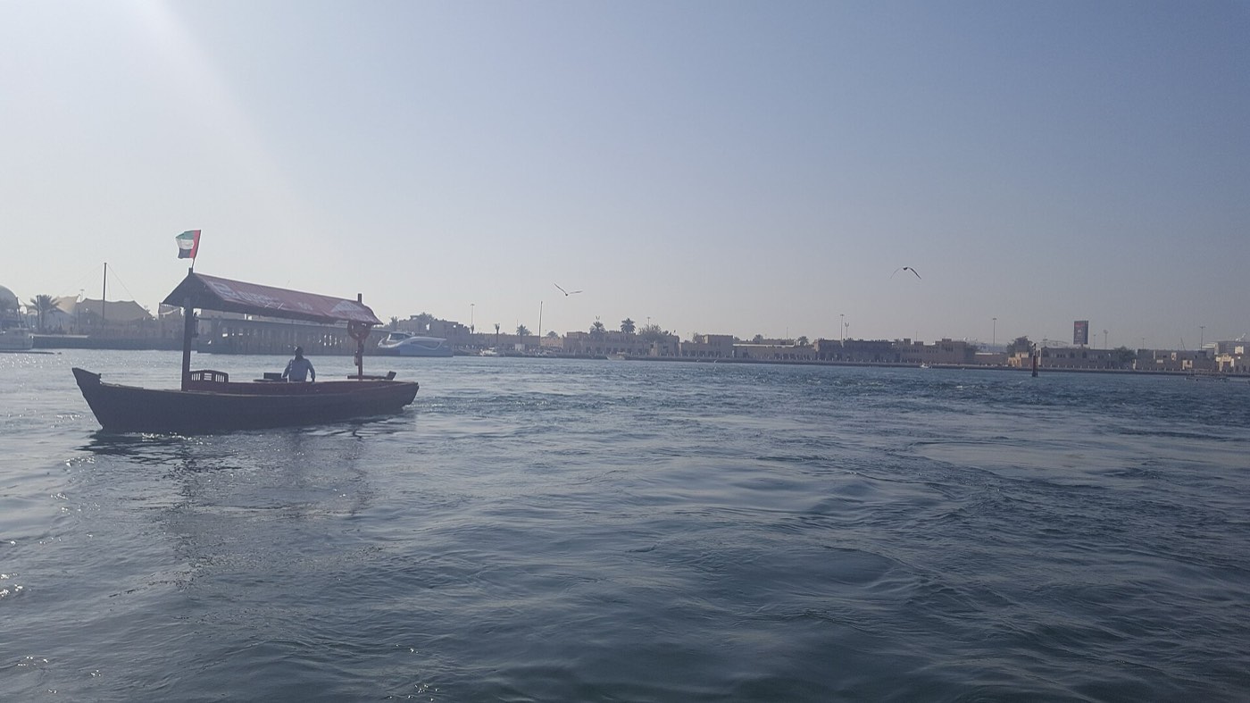 A traditional wooden abra ferry crossing Dubai Creek with the low waterfront buildings of Deira in the background