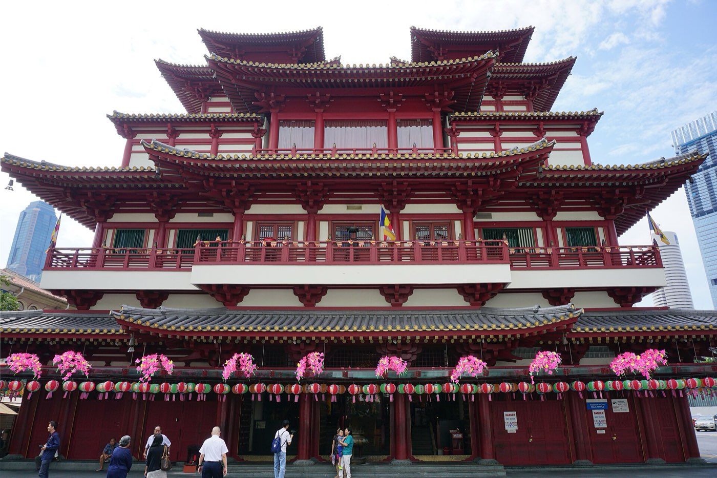 The red-and-gold, multi-tiered facade of the Buddha Tooth Relic Temple in Chinatown, Singapore, decorated with pink floral garlands and lanterns