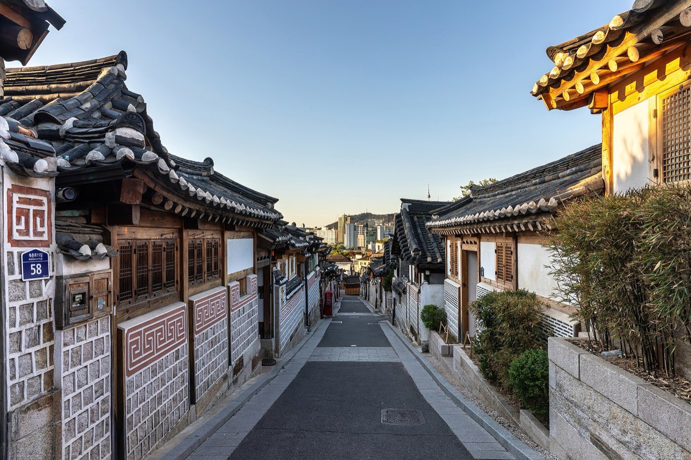 An empty sloped street lined with traditional Korean hanok houses with dark tiled roofs in Bukchon Hanok Village, Seoul, lit by early morning sun
