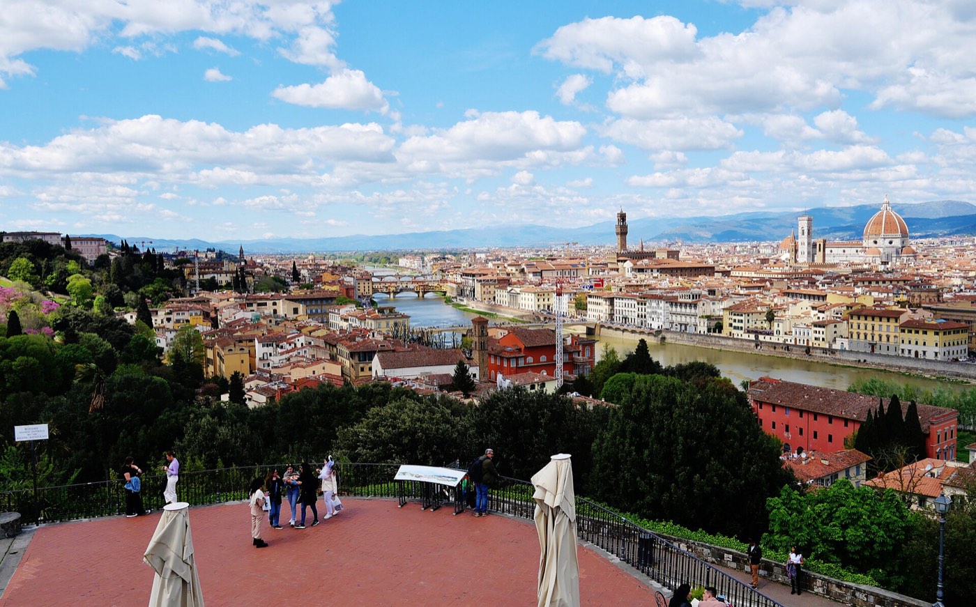 Panoramic view of Florence from Piazzale Michelangelo, with the Ponte Vecchio crossing the Arno and the Duomo's dome and Palazzo Vecchio's tower visible across the rooftops