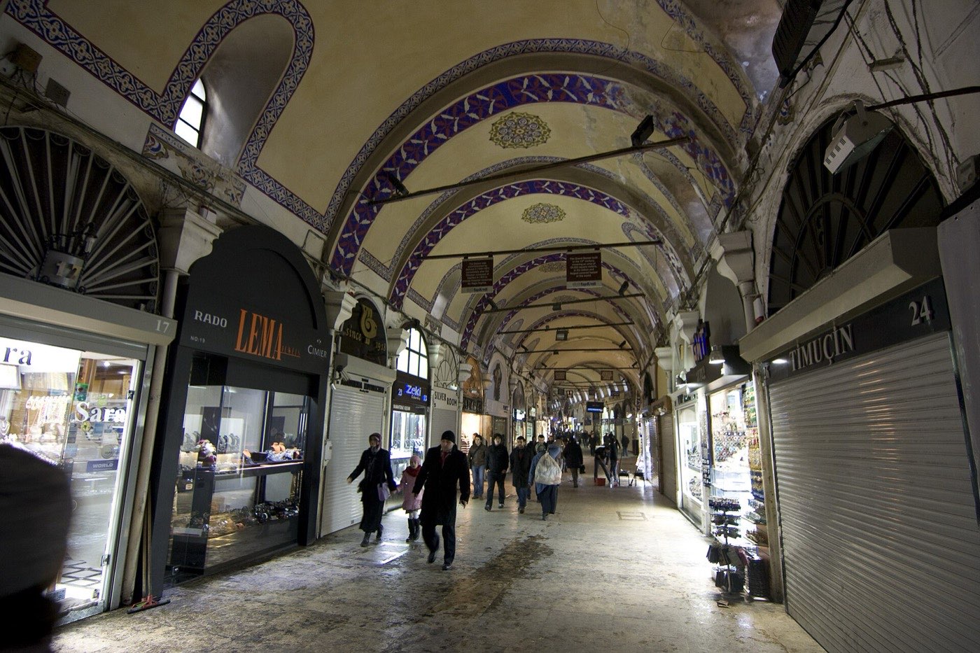 A painted vaulted arcade inside the Grand Bazaar with jewellery shops along both sides and several shutters closed