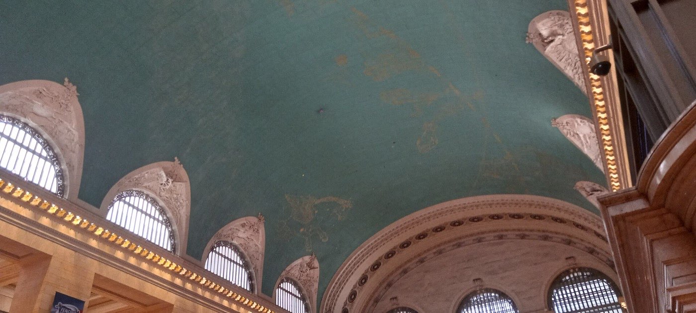 The green painted ceiling of Grand Central Terminal showing faint gilded constellations above a row of arched windows