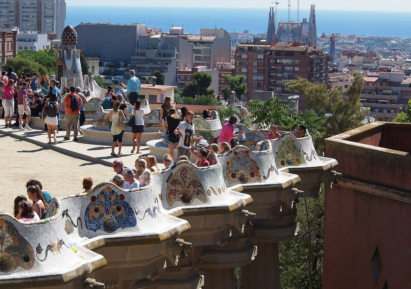 The mosaic-tiled serpentine bench on Park Güell's main terrace, with Barcelona's flat city grid and the sea stretching out below