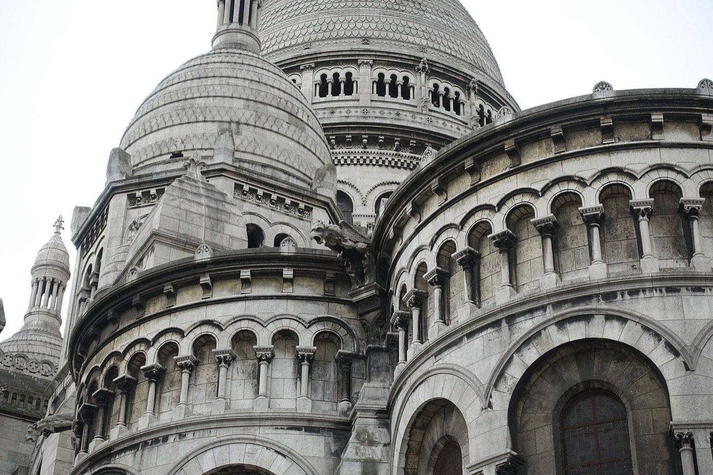 The pale stone domes and arcaded galleries of the Sacré-Cœur basilica photographed from below against a white sky