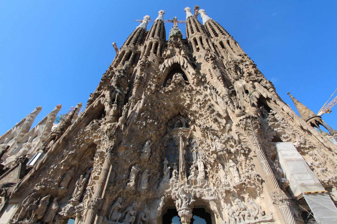 Close-up view of the Sagrada Família's ornately carved stone facade and spires against a clear blue sky in Barcelona