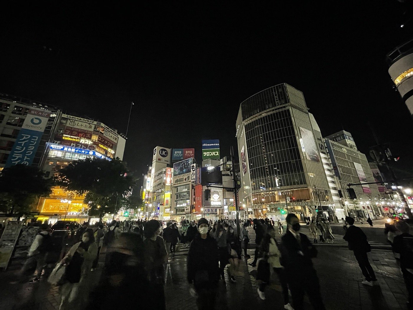 Crowds streaming across the Shibuya scramble crossing at night under lit billboards and office towers