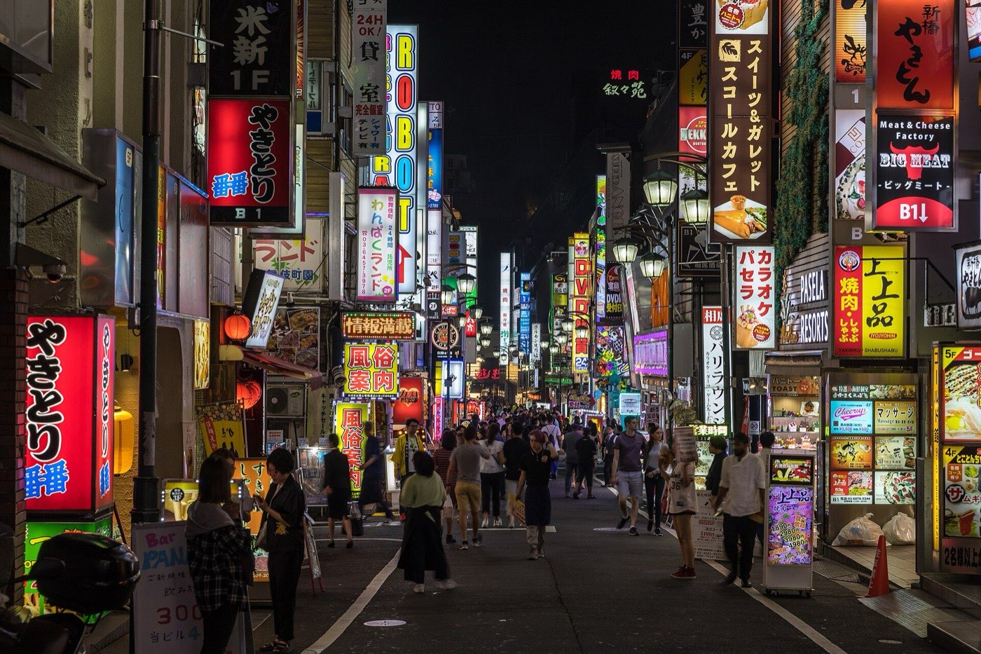 A narrow street in Kabukichō, Shinjuku, walled on both sides with stacked illuminated signs in Japanese and people walking down the middle