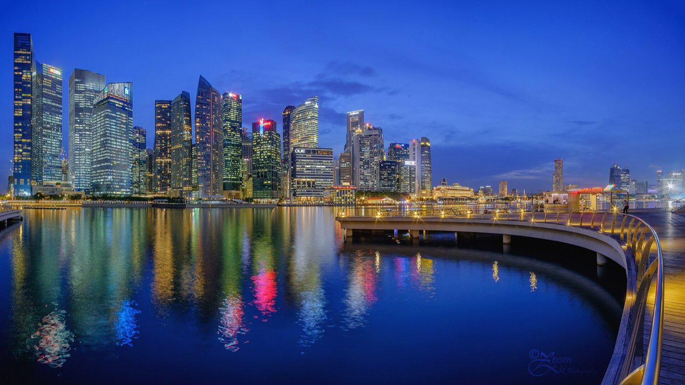 The Downtown Core skyline reflected in Marina Bay at blue hour, seen from the waterfront promenade near Marina Bay Sands