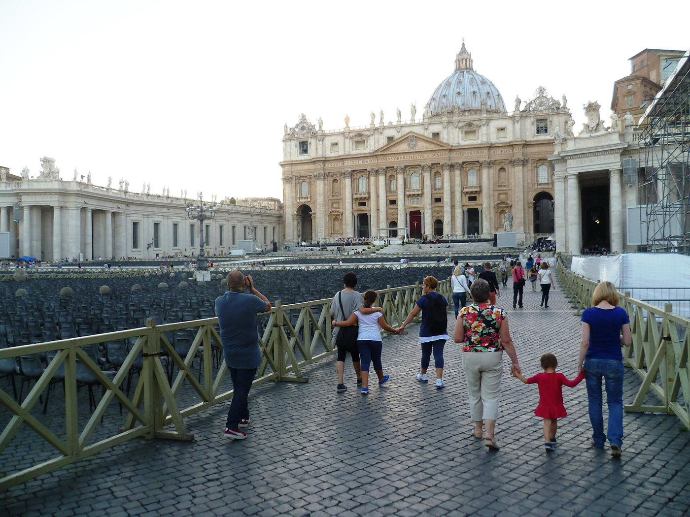 St Peter's Square in Rome with the basilica's dome and facade in the distance, visitors walking along a barriered path in the foreground