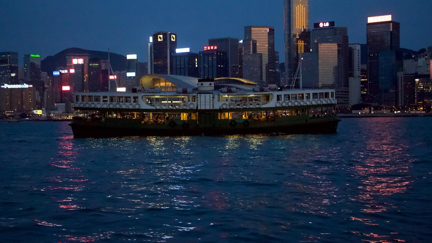 A green-and-white Star Ferry crossing Victoria Harbour at night with the illuminated Hong Kong Island skyline behind it