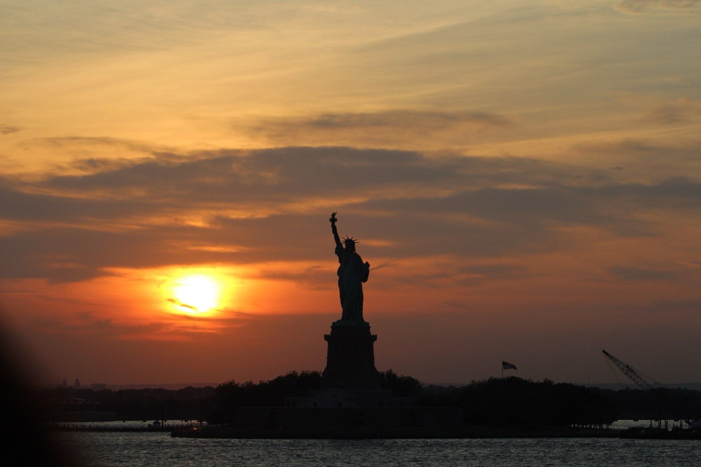 The Statue of Liberty in silhouette against an orange sunset, photographed from the water