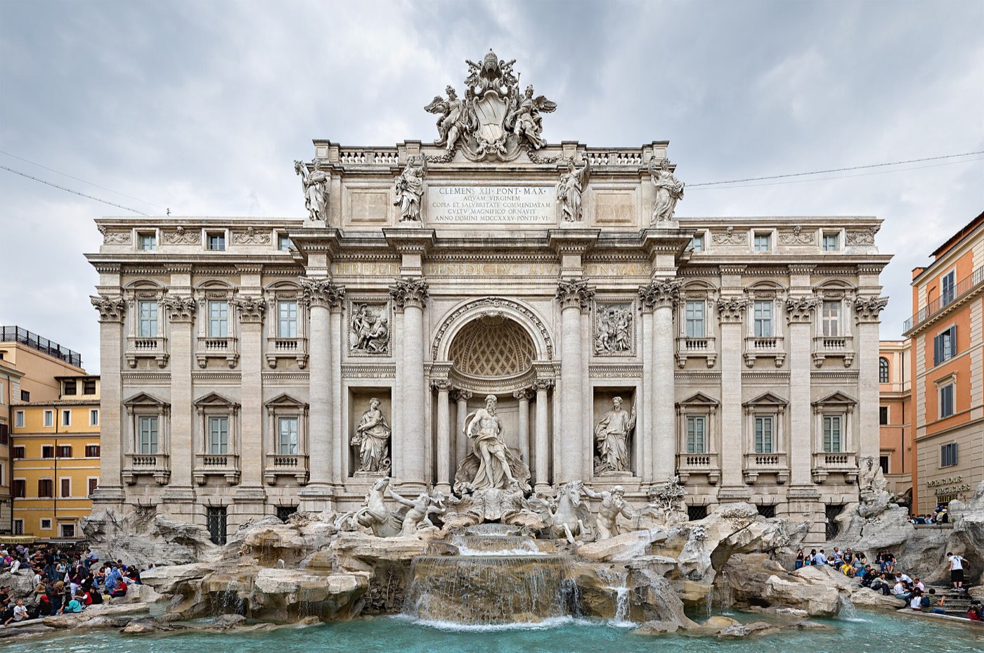 The Trevi Fountain in Rome, its Baroque facade and central statue of Oceanus reflected in the pool, with crowds gathered on the surrounding steps