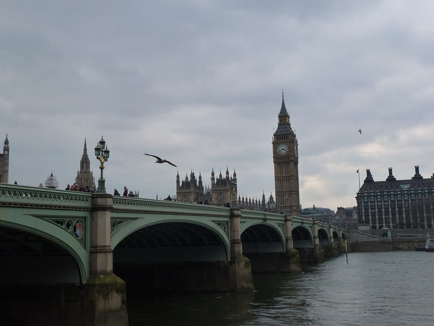 Westminster Bridge and the Elizabeth Tower under heavy grey cloud, with a gull crossing the frame